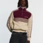 Modelo luciendo el jersey Powerline Zip Knit de Cold Culture en beige y burdeos, con cuello alto de cremallera, mangas amplias y rayas en el pecho.