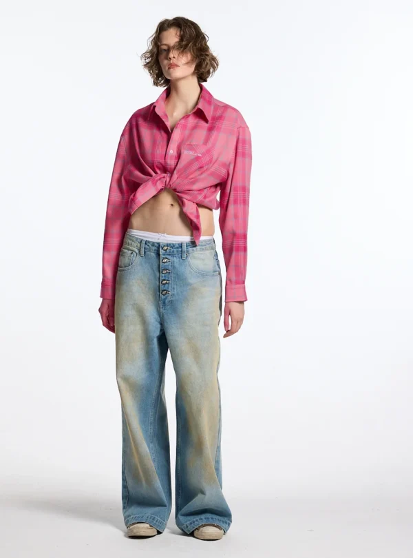 Modelo con camisa Rake rosa de cuadros de Cold Culture anudada a la cintura, con bolsillo delantero y mangas largas, combinada con vaqueros anchos