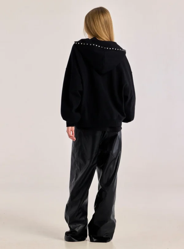 Modelo de espaldas con la sudadera Raw Zip-up Hoodie negra de Cold Culture, mostrando la capucha bajada con tachuelas metálicas y el corte holgado.