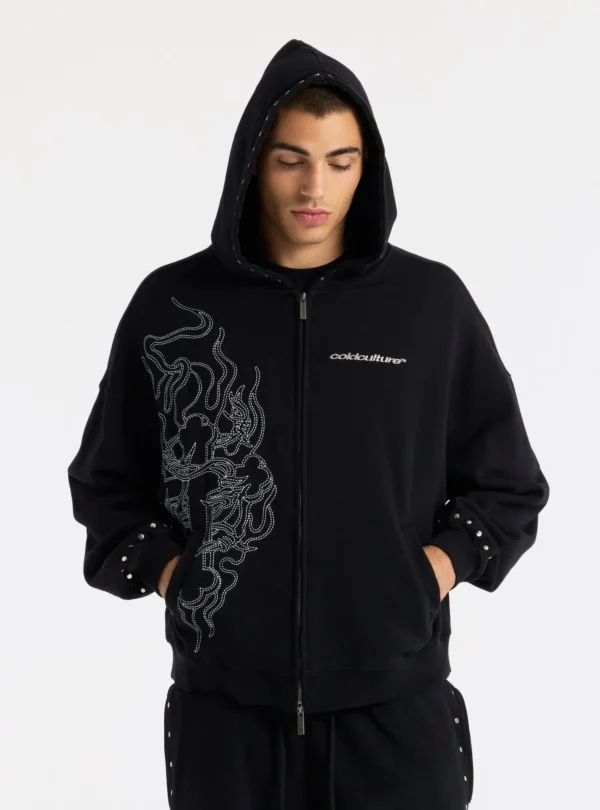 Modelo con la sudadera Raw Zip-up Hoodie negra de Cold Culture, con capucha puesta, cremallera frontal y diseño de líneas blancas.