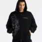 Modelo con la sudadera Raw Zip-up Hoodie negra de Cold Culture, con capucha puesta, cremallera frontal y diseño de líneas blancas.