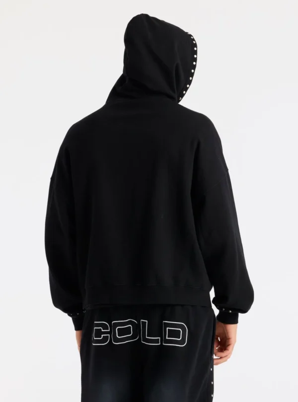 Modelo de espaldas con la sudadera negra Raw Zip-up Hoodie de Cold Culture, con capucha puesta, espalda lisa y detalles metálicos en el borde de la capucha.