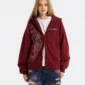 Modelo con sudadera roja Raw Zip-up Hoodie de Cold Culture, abierta sobre una camiseta blanca, con gráfico frontal y logotipo en el pecho.
