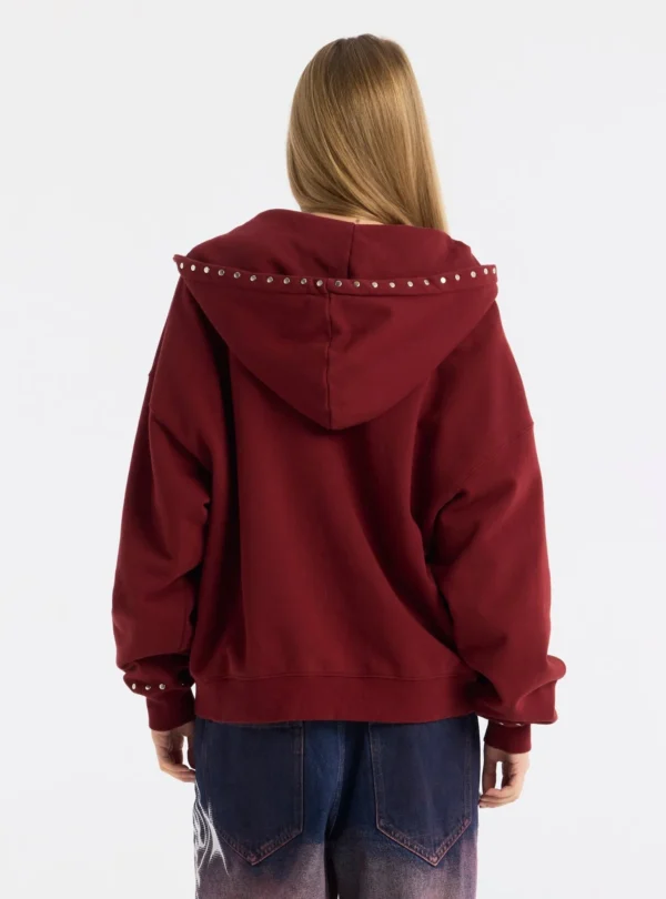 Cold Culture Raw Zip-up Hoodie – Rojo – Vista trasera en modelo Vista trasera de la sudadera roja Raw Zip-up Hoodie de Cold Culture en modelo, con capucha adornada con tachuelas metálicas y corte holgado.