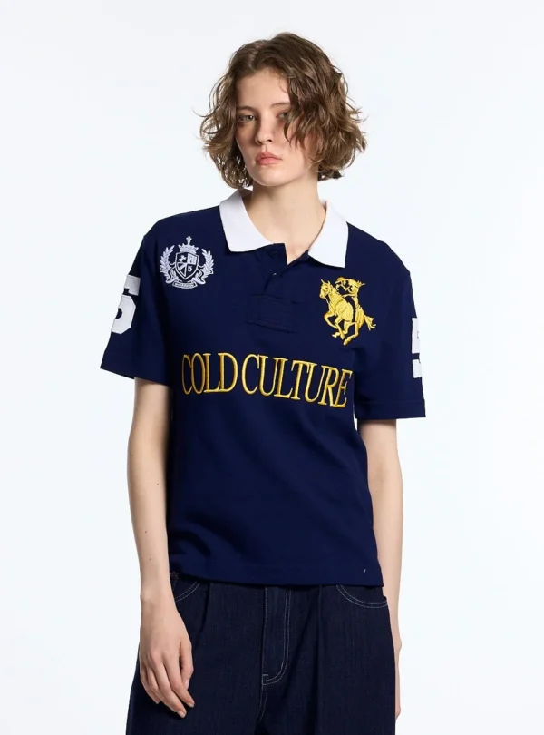 Modelo con polo Riding Club de Cold Culture azul marino, con escudo blanco, bordado ecuestre amarillo y logotipo frontal.