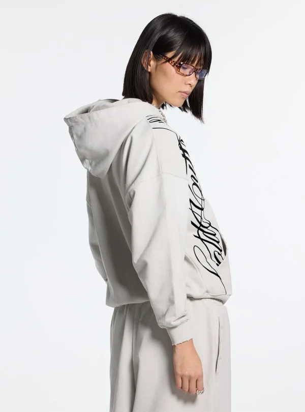 Cold Culture Script Sudadera Con Cremallera – Light Grey – Vista lateral Vista lateral de la sudadera con cremallera Cold Culture Script en gris claro, mostrando el gráfico negro y la capucha