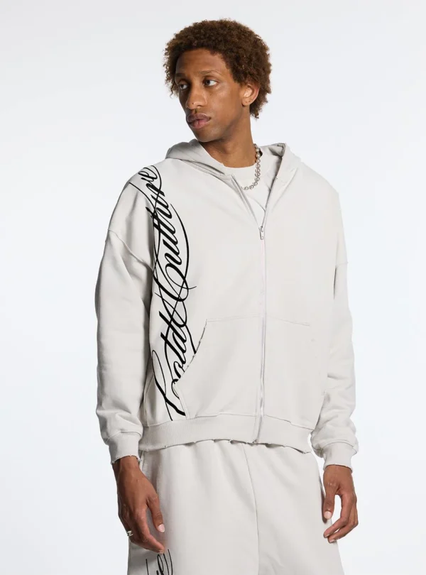 Cold Culture Script Sudadera Con Cremallera – Light Grey – En modelo Modelo con sudadera con cremallera Cold Culture Script en gris claro, mostrando el gráfico negro lateral y los bolsillos delanteros