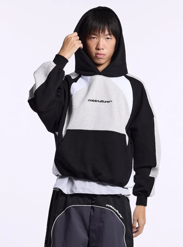 Modelo con la capucha puesta de la sudadera Speed Spoke de Cold Culture en negro y gris jaspeado, con bolsillo canguro y logotipo frontal.