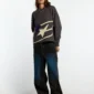 Modelo femenina con jersey Spider Knit gris de Cold Culture, gráfico de araña morada y pantalones anchos oscuros.