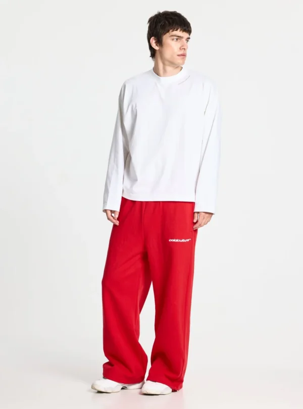 Modelo con pantalones deportivos rojos Stars de Cold Culture de corte ancho, logotipo blanco en la parte delantera y camiseta blanca de manga larga.