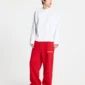 Modelo con pantalones deportivos rojos Stars de Cold Culture de corte ancho, logotipo blanco en la parte delantera y camiseta blanca de manga larga.