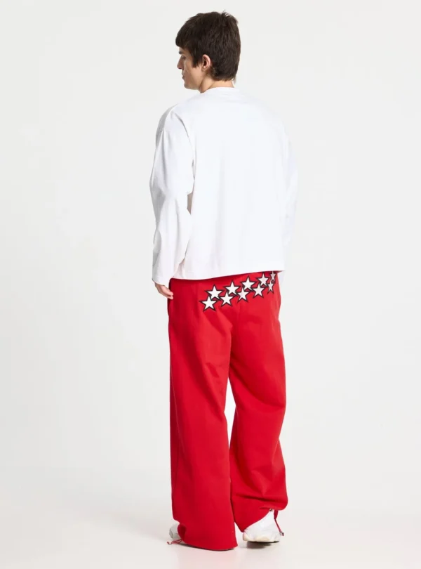 Modelo de espaldas con pantalones deportivos rojos Stars de Cold Culture, con estrellas blancas y negras en la parte trasera y perneras holgadas.