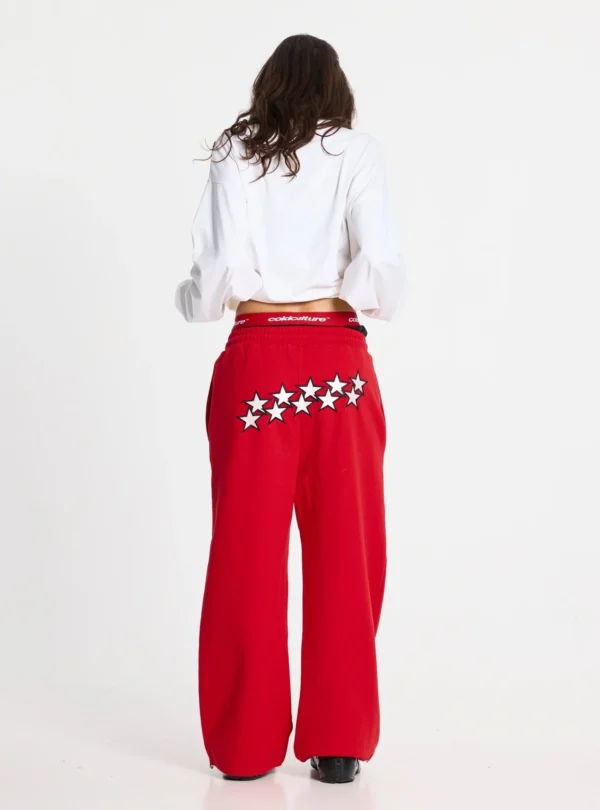 Modelo femenina de espaldas con pantalones deportivos rojos Stars de Cold Culture, decorados con estrellas blancas de borde negro en la parte posterior.