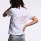 Detalle trasero del polo blanco Starttrail de Cold Culture en modelo masculino, con gráfico Peace de contorno rojo y estrellas azules.