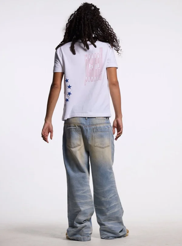 Modelo masculino de espaldas con polo blanco Starttrail de Cold Culture, gráfico Peace rojo y estrellas azules en el lateral.
