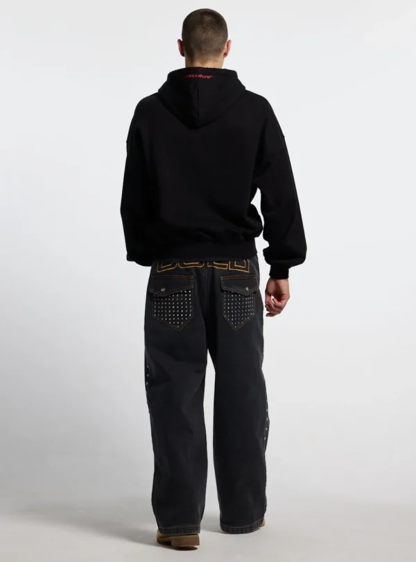 Modelo de espaldas con pantalones Cold Culture Studs en denim negro, bolsillos con tachuelas y bordado COLD