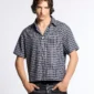 Modelo con camisa Tartan Script negra de Cold Culture, estampado de cuadros, cuello abierto, botones frontales y logotipo blanco en el pecho