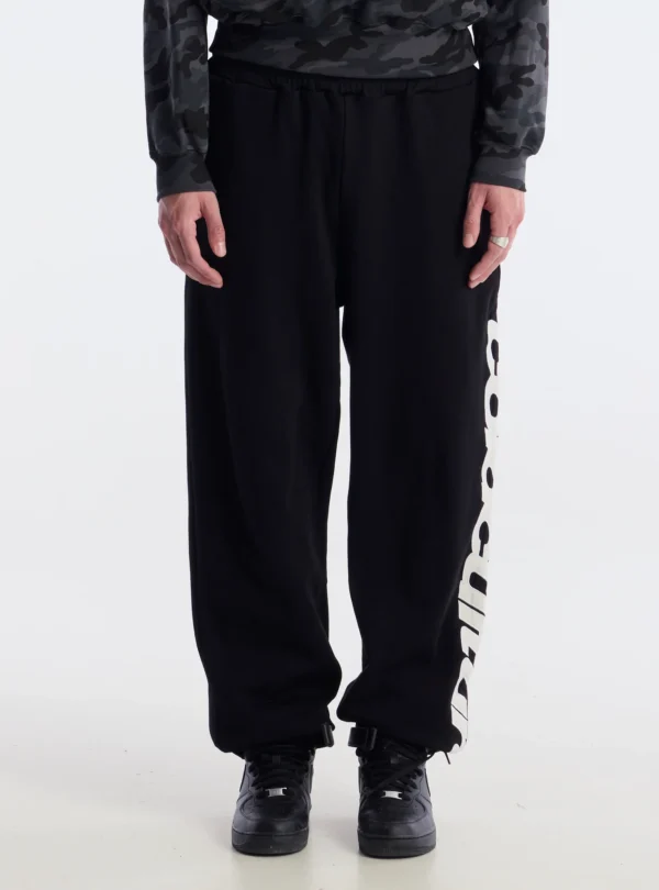 Detalle frontal de los pantalones deportivos Vertical Black de Cold Culture, con perneras anchas, cintura elástica y letras blancas en el lateral.