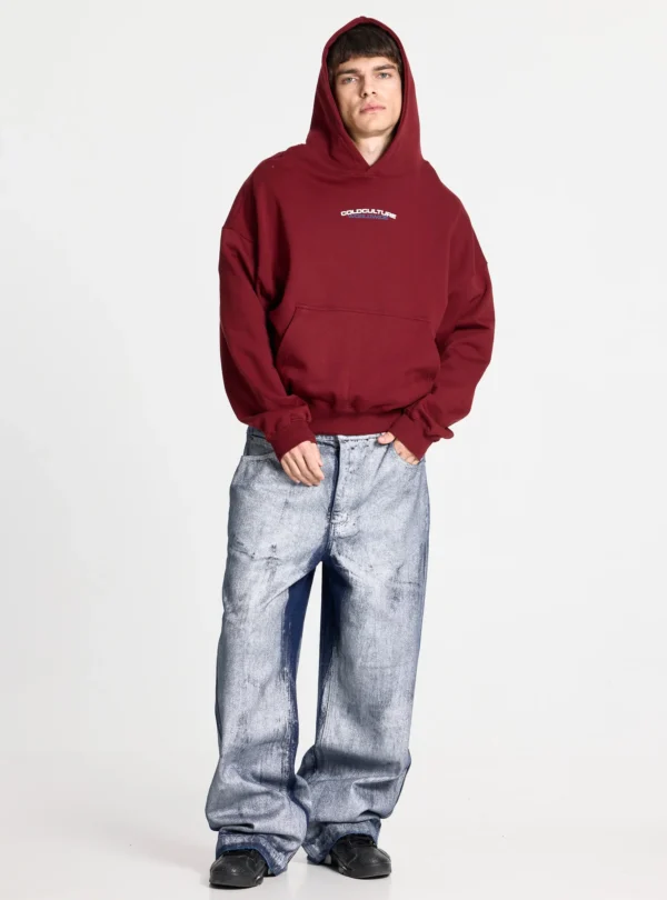 Modelo con pantalones Waxed V2 de Cold Culture en denim lavado, de pernera ancha y acabado desgastado, combinados con una sudadera burdeos y zapatillas negras.