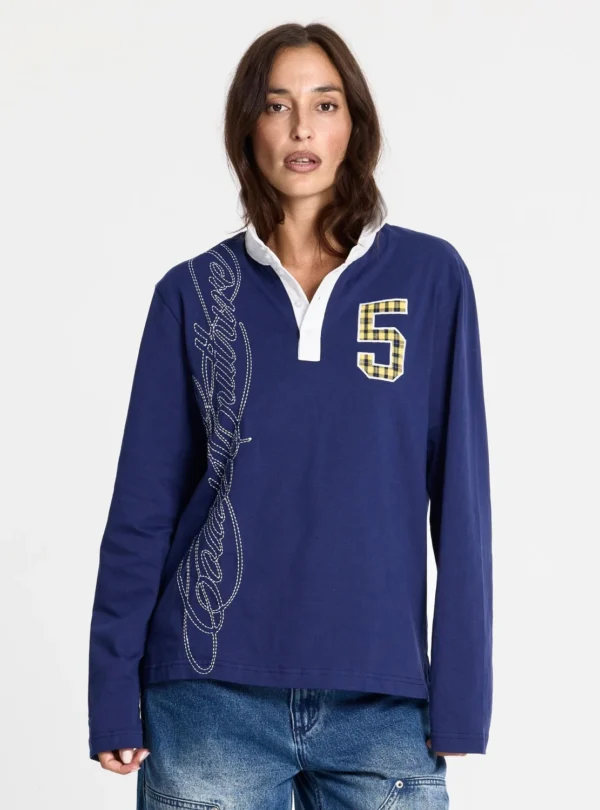 Modelo de frente con el polo Windsor Longsleeve Polo Navy de Cold Culture, azul marino, con mangas largas, cuello blanco y bordado decorativo vertical.